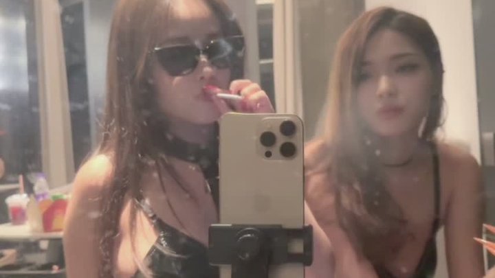 Two sexy Asian girls wearing provocative uniforms, smoking in front of a mirror.